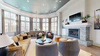 Located at 1810 Arden Creek Pl in Charlottesville, VA, this single-floor space combines sophisticated design with functional living. The open-concept layout seamlessly connects the living and kitchen areas, creating a cohesive and inviting environment throughout.

The living room is a standout space, anchored by a stacked-stone fireplace with a crisp white mantel and a wall-mounted television above. A dramatic tray ceiling finished in deep teal adds a bold architectural focal point, complemented by recessed lighting and an elegant chandelier. Rich hardwood-style flooring runs throughout, grounding the space with warmth and continuity.

A curved bay of floor-to-ceiling windows floods the dining area with abundant natural light, offering views of the surrounding landscape and providing an airy, open ambiance. Patterned drapery frames the expansive glass, adding texture and elegance.

The kitchen is thoughtfully designed with rich dark wood cabinetry, granite countertops featuring subtle veining, and stainless steel appliances including a full-size refrigerator and built-in microwave. Light hardwood floors and white walls keep the space bright and clean, while pendant lighting adds a refined finishing touch.

Together, these spaces deliver a well-balanced blend of architectural character, natural light, and upscale finishes in a compact yet carefully crafted layout.