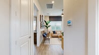 This contemporary single-story residence showcases a harmonious blend of style and functionality. The open-concept layout seamlessly connects the living spaces, creating a fluid and airy atmosphere. The living room is adorned with coastal-inspired artwork, rattan chairs, and a plush sofa, all resting on a neutral area rug. 

The kitchen is a chef's dream, boasting white cabinetry, stainless steel appliances, and a spacious island with seating. Large windows and sliding glass doors in the kitchen area flood the space with natural light and offer views of the outdoor patio.

The bedrooms are designed for comfort and relaxation. The master bedroom features a statement blue accent wall, a modern wooden headboard, and coordinating blue and white bedding. A second bedroom continues the coastal theme with blue artwork and rattan accents.

Bathrooms are sleek and contemporary, with white vanities, large mirrors, and glass-enclosed showers. The consistent use of wood-look flooring throughout the home adds warmth and continuity to the space.

Thoughtful details such as recessed lighting, ceiling fans, and carefully curated decor pieces elevate the overall design, creating a sophisticated yet inviting home environment.