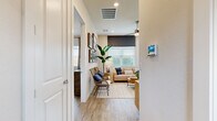 This contemporary single-story residence showcases a harmonious blend of style and functionality. The open-concept layout seamlessly connects the living spaces, creating a fluid and airy atmosphere. The living room is adorned with coastal-inspired artwork, rattan chairs, and a plush sofa, all resting on a neutral area rug. 

The kitchen is a chef's dream, boasting white cabinetry, stainless steel appliances, and a spacious island with seating. Large windows and sliding glass doors in the kitchen area flood the space with natural light and offer views of the outdoor patio.

The bedrooms are designed for comfort and relaxation. The master bedroom features a statement blue accent wall, a modern wooden headboard, and coordinating blue and white bedding. A second bedroom continues the coastal theme with blue artwork and rattan accents.

Bathrooms are sleek and contemporary, with white vanities, large mirrors, and glass-enclosed showers. The consistent use of wood-look flooring throughout the home adds warmth and continuity to the space.

Thoughtful details such as recessed lighting, ceiling fans, and carefully curated decor pieces elevate the overall design, creating a sophisticated yet inviting home environment.