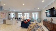 Located at 116 Dapple Ct in Wilmington, NC, this well-appointed single-floor space is designed for comfort and functionality, offering an open, airy layout bathed in natural light. The interior features light-toned hardwood-style flooring, crown molding, and recessed lighting throughout, creating a cohesive and polished aesthetic.

The expansive main lounge area serves as the centerpiece of the space, anchored by a navy tufted sofa accented with warm coral pillows, complemented by a pair of seafoam accent chairs and a wall-mounted flat-screen television above a richly grained wood credenza. Multiple sets of French doors line the rear wall, allowing abundant natural light to pour in while providing direct access to an outdoor area.

The kitchen is equally impressive, featuring a large granite-topped island with bar seating, white shaker cabinetry, a teal tile backsplash, stainless steel appliances, and pendant lighting. A dedicated beverage station adds convenience and functionality to the space.

A casual dining nook with high-top tables and bar stools is positioned near additional French doors and windows, offering views of the outdoors. Throughout the space, coastal-inspired artwork and décor reinforce a relaxed, welcoming ambiance well-suited to Wilmington's coastal character.