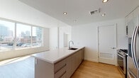 Located in the heart of South Park, Downtown Los Angeles, this modern single-floor residence at 1133 S Hope St offers a sleek, contemporary design throughout. The open-concept layout is anchored by a well-appointed kitchen featuring a large center island with a white quartz countertop, taupe cabinetry extending to the ceiling, a tiled backsplash, and a full suite of stainless steel appliances including a gas range, microwave, and French door refrigerator. Light wood flooring flows seamlessly across the living areas, complementing the bright, white walls and recessed lighting overhead. The living area is bathed in natural light from expansive floor-to-ceiling windows that frame striking views of the Downtown Los Angeles skyline. Additional rooms offer generous proportions, each with large windows that capture city and neighboring building views. The space includes two well-designed bathrooms — one featuring a glass-enclosed walk-in shower with large-format tile flooring, and a second with a soaking tub-shower combination, both finished with white quartz vanities and large mirrors. Clean lines, neutral tones, and abundant natural light define the overall ambiance of this urban residence.