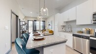 Located in Fort Worth, TX, this well-designed 2-bedroom, 2-bathroom residence offers a thoughtful layout with modern finishes throughout. The open-concept kitchen is a standout feature, showcasing crisp white cabinetry, granite countertops with a subtle grey veining, a penny-tile backsplash, and a full suite of stainless steel appliances including a range, microwave, dishwasher, and refrigerator. A large kitchen island with seating provides an ideal space for casual dining and entertaining, illuminated by stylish pendant lighting. The kitchen flows seamlessly into the living area, which benefits from large windows that invite natural light and views of the outdoors. Both bedrooms are comfortably sized, with the primary bedroom featuring tall ceilings, wood-look flooring, and direct access to its en-suite bathroom. The en-suite bath offers a double vanity with granite countertops, white cabinetry, and a tiled soaking tub-shower combination. The second bathroom mirrors this clean aesthetic with subway tile surround and wood-look flooring. Each bedroom includes a dedicated closet with built-in shelving for organized storage. Light-toned wood-look flooring runs throughout the home, tying together a cohesive, contemporary look.