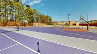 Located at Berkeley Place in Clemson, South Carolina, this outdoor recreational facility offers a well-designed multi-sport court complex suited for a variety of athletic activities. The courts feature a striking purple and orange color scheme — a nod to Clemson's iconic team colors — with crisp white court markings laid out across a smooth, durable playing surface.

The basketball court is a standout feature, spanning a generous full-court layout complete with regulation hoops, painted key areas, and clearly defined boundary lines. A central court area doubles as a tennis and pickleball court, equipped with a net system and proper court markings to accommodate both sports simultaneously or separately.

The facility is fully enclosed by a chain-link perimeter fence, providing a secure and defined play environment. Multiple tall light poles are strategically positioned throughout the complex, ensuring the courts are well-lit for evening use. The surrounding landscape features mature trees that provide a natural backdrop, while the open sky overhead allows for abundant natural light during daytime play.

The setting within an established residential neighborhood adds a community-oriented atmosphere to the facility, making it an accessible and versatile recreational asset for residents. The combination of multi-sport functionality, durable court surfaces, and thoughtful amenities makes this an excellent year-round outdoor sporting destination.