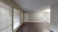 This single-story space is finished with a consistent, modern aesthetic throughout. Dark hardwood-style flooring runs across all rooms, creating a rich contrast against the neutral gray walls and bright white trim and baseboards. The main living areas are open and well-proportioned, with ample natural light provided by large windows dressed with horizontal blinds. Ceiling-mounted HVAC vents are present throughout, ensuring efficient climate control.

The galley-style kitchen is a standout feature, equipped with dark cabinetry, granite-patterned countertops, a subway tile backsplash, a double-basin sink, and stainless steel appliances including a refrigerator, electric range, dishwasher, and built-in microwave. An electrical panel is also accessible within the kitchen area.

The bedrooms each include ceiling fans with light fixtures and generous closet space — one bedroom features a walk-in closet, while another offers dual reach-in closets with bifold doors. Windows in the bedrooms allow for natural light and outdoor views.

The bathroom is well-appointed with dark cabinetry, a granite-topped vanity, a framed mirror, and a stand-alone shower with a frosted glass door. The entry area features vertical shiplap-style wall paneling, adding a subtle design detail near the front door.
