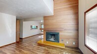 Located at 1884 Happy Ln in Eugene, Oregon, this two-story home offers 2 bedrooms, 2 bathrooms, and a well-considered layout spread across two floors. The main level sets a welcoming tone with an open living room anchored by a striking wood-paneled fireplace wall with a yellow tiled hearth — a standout architectural detail that adds warmth and mid-century character. Hardwood-style flooring flows throughout the main level, complementing the neutral palette. Natural light filters in through multiple windows, and the open sightlines between the living area and kitchen create a connected, functional flow. The kitchen features warm wood cabinetry, a full-size refrigerator, and direct access to the staircase. A dedicated laundry nook with overhead cabinetry and washer/dryer hookups adds everyday convenience. Upstairs, the generously sized primary bedroom is carpeted and connects to a private en-suite bathroom equipped with a walk-in shower and built-in linen shelving. The second bedroom features sloped ceilings, a wood-paneled accent wall, and a window with a view of surrounding greenery. Two closets and a hallway complete the upper floor. Textured ceilings, warm wood trim, and louvered doors carry cohesive design details throughout the home.