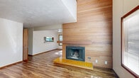 Located at 1884 Happy Ln in Eugene, Oregon, this two-story home offers 2 bedrooms, 2 bathrooms, and a well-considered layout spread across two floors. The main level sets a welcoming tone with an open living room anchored by a striking wood-paneled fireplace wall with a yellow tiled hearth — a standout architectural detail that adds warmth and mid-century character. Hardwood-style flooring flows throughout the main level, complementing the neutral palette. Natural light filters in through multiple windows, and the open sightlines between the living area and kitchen create a connected, functional flow. The kitchen features warm wood cabinetry, a full-size refrigerator, and direct access to the staircase. A dedicated laundry nook with overhead cabinetry and washer/dryer hookups adds everyday convenience. Upstairs, the generously sized primary bedroom is carpeted and connects to a private en-suite bathroom equipped with a walk-in shower and built-in linen shelving. The second bedroom features sloped ceilings, a wood-paneled accent wall, and a window with a view of surrounding greenery. Two closets and a hallway complete the upper floor. Textured ceilings, warm wood trim, and louvered doors carry cohesive design details throughout the home.