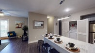 This well-appointed 4-bedroom, 4-bathroom single-floor residence offers a thoughtfully designed layout ideal for shared or family living. The open-concept kitchen is a standout feature, showcasing dark cabinetry, stainless steel appliances, a mosaic tile backsplash, granite-style countertops, and a large breakfast bar with seating for multiple guests. The kitchen flows seamlessly into the living area, which is brightened by multiple windows, hardwood-style flooring, and a ceiling fan overhead. A welcoming entryway with practical wall storage sets the tone upon arrival. Each of the four bedrooms is carpeted for comfort and includes windows that invite natural light, with some rooms featuring tray ceilings that add architectural interest. The four bathrooms are consistently finished with granite-topped dark vanities, undermount sinks, and large mirrors. Bathrooms feature either shower-tub combinations with tile flooring or en-suite configurations adjacent to bedrooms. A dedicated in-unit laundry area adds everyday convenience. The overall color palette of warm neutrals and gray tones creates a cohesive, modern ambiance throughout the residence.