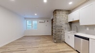 This thoughtfully designed bi-level residence spans two floors, offering a compelling mix of historic architectural elements and contemporary updates throughout. The lower level serves as the main living and kitchen area, immediately distinguished by a dramatic exposed stone masonry column that anchors the open-concept space. Light wood-tone flooring runs continuously throughout both levels, complementing the clean white walls and recessed lighting. A wall-mounted mini-split system provides climate control, and a window brings in natural light.

The kitchen is well-appointed with white shaker cabinetry, quartz countertops, a subway tile backsplash, and a full suite of stainless steel appliances including a dishwasher, range, microwave, and refrigerator. A striking black spiral staircase connects the lower level to the more expansive upper floor, where both bedrooms, two full bathrooms, and in-unit stacked laundry are located. The primary bedroom features a window with views of the surrounding stone exterior facade, while the second bedroom offers a clean, functional layout. One bathroom includes a tiled tub-shower combination, while the second features a frameless glass walk-in shower, both finished in crisp white tile with light stone-look flooring.