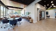 Located at 2000 Riverside Dr in Richmond, Virginia, this single-floor commercial space combines contemporary design with a welcoming, energetic atmosphere. The entrance features floor-to-ceiling glass walls and automatic sliding doors that flood the entryway with natural light, offering clear views of the surrounding greenery and parking area. Light-toned tile flooring and sleek linear ceiling fixtures set a clean, professional tone from the moment of arrival.

Moving inside, the space opens into a vibrant lounge and reception area highlighted by a bold, honeycomb-patterned green ceiling installation that serves as a striking focal point. A textured white 3D wall panel anchors a seating area furnished with deep red accent chairs and a patterned rug, alongside original colorful artwork. Collaborative high-top workstations and open corridors make the space highly functional for both social interaction and productivity.

A relaxed lounge area benefits from expansive windows that frame lush outdoor views, complemented by a warm wood-panel ceiling, built-in shelving, and a convenient refreshment station with stocked refrigerators. Comfortable seating arrangements and curated décor add to the inviting ambiance.

Additional areas showcase a media wall with a built-in linear fireplace, flat-screen television, and custom cabinetry, as well as intimate seating vignettes adorned with large-scale abstract artwork and rich leather sofas, reflecting a thoughtfully curated, design-forward environment throughout.