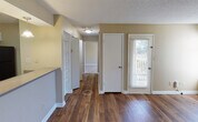 This single-floor residence on SR-255 N in Huntsville, Alabama offers a well-organized layout with a cohesive design throughout. Warm-toned walls and rich hardwood flooring run through the main living areas, creating an inviting atmosphere from entry to hallway. The living area is generously proportioned and includes a built-in desk and open shelving unit, providing functional storage and workspace along one wall. Natural light enters through multiple windows fitted with horizontal blinds, offering pleasant outdoor views.

The kitchen is arranged in a galley-style configuration and opens to the living space via a peninsula counter with pendant lighting overhead. White cabinetry, a double-basin sink, and black appliances—including a refrigerator, electric range, and microwave—are neatly organized along both walls, with hardwood flooring continuing underfoot.

A hallway connects the sleeping areas and bathrooms. The bedroom features plush carpeting, a window with natural light, and a textured ceiling. The bathroom area includes a vanity with white cabinetry, a large mirror, and a separate wet area housing a tiled soaking tub and shower combination. An exterior door provides access to an outdoor area, adding convenience and connectivity to the outside.