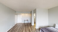 This single-floor unit offers a well-organized layout with a cohesive, modern aesthetic carried throughout each room. The living area greets you upon entry with warm wood-look plank flooring, light gray walls, and a textured ceiling that adds subtle character. A front entry door with a closet is positioned near a built-in accent shelf, while a wall-mounted HVAC unit and horizontal blinds along a large window provide both comfort and natural light control.

The kitchen is efficiently designed with crisp white shaker-style cabinetry extending to the ceiling for ample storage. White quartz-style countertops, a subway tile backsplash, a stainless steel double-basin sink with a brushed nickel faucet, and a Whirlpool refrigerator complete this clean, functional space.

The bedroom is generously proportioned, featuring the same wood-look flooring, two windows dressed with blinds, and a wall-unit HVAC system. The room offers an open, airy feel and direct access to the bathroom.

The bathroom is finished in a light, neutral palette with wood-look tile flooring, a white vanity with an undermount sink, a toilet, and a shower-tub combination enclosed by a white curtain. Overhead lighting and a ventilation fan complete the space. Overall, the unit presents a fresh, move-in-ready environment with consistent, contemporary finishes.