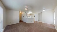 This single-floor residential unit offers a practical and comfortable layout centered around an open-concept living and dining area. The spacious living room is finished with plush wall-to-wall carpeting and features a ceiling fan with integrated lighting. A large window allows natural light to fill the room while providing views of surrounding greenery outdoors. The kitchen is positioned at the heart of the unit, defined by a peninsula counter that separates it from the living area. It is equipped with light wood cabinetry, white appliances including a refrigerator, electric range, over-the-range microwave, and dishwasher, alongside wood-look flooring and ample counter space. The bedrooms are generously sized, each featuring plush carpeting, ceiling fans, and windows that bring in natural light and outdoor views. A standout feature is the walk-in closet, offering substantial storage with wrap-around shelving. The unit includes two full bathrooms, each equipped with a tub-shower combination. One bathroom showcases wood-look flooring and light wood vanity cabinetry with a single sink, while the other is finished with clean white surfaces and wood-look flooring. Throughout, the interiors are finished in neutral tones, creating a bright and cohesive atmosphere.