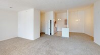This single-story residence offers a practical and well-organized layout across two bedrooms, two full bathrooms, and a den. The living area is expansive and carpet-floored, bathed in natural light through large sliding glass doors and an additional window, creating a bright and open atmosphere. The space flows seamlessly toward the kitchen, which is separated by a peninsula counter and illuminated by a chandelier overhead. The kitchen is outfitted with warm wood cabinetry, white appliances including a refrigerator, range, and dishwasher, along with a stainless steel sink and light-toned countertops over tile flooring.

Both bedrooms are carpeted and include ceiling fans with lighting. The primary bedroom features access to a private en-suite bathroom and a walk-in closet, providing ample storage. The second bedroom is similarly sized with a ceiling fan and a window for natural light. Each bathroom includes a wood-tone vanity, broad mirror, and tile flooring. One bathroom conveniently connects to an in-unit laundry area equipped with a full-sized washer and dryer. The den adds flexible space suitable for a home office or additional living area.