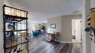 This single-floor residence offers a thoughtfully organized layout that balances comfort and functionality throughout. The open-plan living area is finished with durable wood-look flooring in a cool grey tone, neutral wall colors, and a textured ceiling, creating a bright and welcoming atmosphere. The living space accommodates a seating arrangement centered around a low coffee table, with natural light filtering in through large windows fitted with vertical blinds.

Adjacent to the living area, a dedicated dining space features a solid wood table with upholstered chairs and is accented by a large framed abstract artwork. A functional workspace area with a writing desk and seating provides a productive zone within the open floor plan, complemented by an industrial-style wire shelving unit that adds character.

The kitchen is well-equipped with crisp white shaker-style cabinetry, marble-patterned countertops, stainless steel appliances including a range, microwave, and dishwasher, and a modern matte black faucet — offering both style and practicality.

The bedroom is carpeted for comfort and features a large sliding glass door with vertical blinds that allows ample natural light and outdoor access. A closet and additional storage complete the room. Throughout, the space maintains a cohesive, clean aesthetic with carefully chosen furnishings and decorative touches.