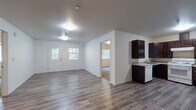 Located at 507 East Cope Industrial Way in Palmer, Alaska, this single-floor unit offers a clean, functional layout designed for comfortable living. The open-concept living and dining area is anchored by durable wood-look plank flooring that extends throughout the main living spaces, complemented by bright white walls and natural light streaming in through multiple windows. The front entry leads directly into this expansive area, creating a welcoming and airy atmosphere.

The kitchen is well-equipped, featuring rich dark wood cabinetry with brushed nickel hardware, light granite countertops, a full suite of appliances including a range with overhead hood, and a dishwasher. Ample cabinet space and a generous countertop footprint make this kitchen both practical and visually appealing.

The bedrooms are finished with plush wall-to-wall carpeting and each includes a window offering serene views of the surrounding wooded landscape, filling the rooms with natural light and a sense of connection to the outdoors. Closet access is conveniently integrated into the hallway layout.

The bathroom is thoughtfully designed with accessibility in mind, featuring grab bars at the tub and shower, a handheld showerhead, a vanity with under-counter clearance, granite countertop, and wood-look flooring. The overall finish of the unit is clean and contemporary throughout.