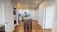 This single-floor residence offers a thoughtfully designed layout that balances functionality and comfort throughout. Rich, dark hardwood-style flooring flows consistently across all living areas, anchoring the space with warmth and visual continuity.

The kitchen is a standout feature, outfitted with a full suite of stainless steel appliances — including a refrigerator, electric range, over-the-range microwave, and dishwasher — set against crisp white cabinetry and light granite-style countertops. A freestanding kitchen island with a butcher block top and bar seating provides additional prep space and casual dining. Conveniently tucked nearby is a stacked in-unit washer and dryer, adding everyday practicality.

The living area is bright and open, accented by wainscoting along the walls that lends a refined architectural touch. Natural light enters through large windows, offering views of the surrounding area.

Two bedrooms provide comfortable accommodations, each featuring closets with wire shelving systems. One bedroom includes a ceiling fan and a window with an outdoor view, while the other enjoys direct access to the bathroom. The bathroom is clean and functional, featuring a sliding glass-door shower with tiled surround, a white vanity with granite-style countertop, and light tile flooring. The entry foyer includes an accessible electrical panel, completing this well-organized and move-in-ready residence.