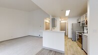 Located at 1221 Mottman Rd SW in Tumwater, Washington, this single-floor residence offers a clean, modern aesthetic with thoughtfully updated finishes throughout. The open-concept layout connects the kitchen and living areas seamlessly, creating a bright and functional flow. The kitchen is well-appointed with gray shaker-style cabinetry, white countertops, a subway tile backsplash, stainless steel appliances including a refrigerator, electric range, microwave, and dishwasher, and light wood-look flooring that extends through the main living spaces. A peninsula with a sink adds additional prep space and serves as a natural divider between the kitchen and living room. The living room is a generous, light-filled space featuring vaulted ceilings, plush carpeting, a fireplace with a clean-lined surround, and large sliding glass doors that open to an outdoor area, inviting natural light from multiple directions. A ceiling fan adds to the comfort of the space. The bedroom area is carpeted and spacious, also featuring a ceiling fan and access to an outdoor balcony through sliding glass doors. The bathroom features a gray vanity with white countertop, framed mirror, and light wood-look flooring, maintaining the cohesive neutral palette found throughout the unit. Ample closet storage is provided in the hallway areas.