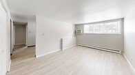 Located at 1136 Vine St in Liverpool, NY, this 3-bedroom, 1-bathroom unit offers a practical and well-organized single-floor layout. Light-toned hardwood flooring runs throughout the entire space, lending a clean, cohesive aesthetic to every room. The neutral gray and white walls provide a bright, airy feel that makes the most of the available square footage.

The generously sized primary bedroom offers notable floor space and features a window that allows natural light to filter in, along with baseboard heating for year-round comfort. The two additional bedrooms are well-proportioned, each with white interior doors and the same consistent flooring found throughout the unit.

The galley-style kitchen is efficiently arranged with white cabinetry lining both sides, a coil electric range, a full-size refrigerator, and a double-basin sink with ample counter space — ideal for everyday cooking needs. The full bathroom includes a shower-tub combination, toilet, and a wood-toned vanity, all finished in clean white surroundings.

A hallway connects the main living areas, and the spacious living area features a window-mounted air conditioning unit, a large window for natural light, and baseboard heating. The primary bedroom also includes a double-door closet, adding practical storage to this well-appointed unit.