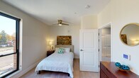 Located at 207 S Mitchell St in Cadillac, Michigan, this single-floor unit offers a thoughtfully designed open layout that combines comfort and functionality. Large, black-framed windows flood the main living and sleeping area with abundant natural light while framing views of the surrounding downtown Cadillac streetscape. Light wood-tone flooring runs throughout, contributing to a clean and cohesive aesthetic.

The kitchen is well-appointed with white shaker-style cabinetry, dark hardware, and a classic white subway tile backsplash. Stainless steel appliances — including a range, over-the-range microwave, and dishwasher — are complemented by dark countertops. A stacked washer and dryer unit is conveniently integrated into the kitchen area, adding practical in-unit laundry access.

The bedroom is a calm and comfortable retreat, featuring light neutral walls, light wood flooring, and a ceiling fan with integrated lighting. A closet provides ample storage, and the room is accented by warm bedside lighting.

The bathroom is finished in a soothing blue-green palette with a combined tub and shower enclosure featuring sliding glass doors, grab bars, a white vanity with an undermount sink, and wood-look tile flooring.

A bold blue entry door adds a distinctive design touch, setting an inviting tone from the moment of arrival. The unit is a well-rounded space ideal for everyday living in a convenient downtown location.