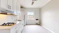 Located on the second floor at 5014 Melrose Ave in the heart of Los Angeles, this studio unit offers a thoughtfully organized layout across a single floor. The bedroom is the primary living space, featuring soft neutral wall tones, crown molding, and light gray tile flooring that mimics the look of hardwood, lending a clean and modern aesthetic throughout. The space is finished with crisp white baseboards that complement the understated color palette.

The kitchenette area is well-appointed with white shaker-style cabinetry, brushed nickel hardware, and a light stone-look countertop. A gas cooktop with an overhead range hood provides functional cooking capability, while upper and lower cabinets offer ample storage. A full-size refrigerator fits neatly within the kitchen footprint. A window in the kitchen area allows natural light to filter in, offering a view of the surrounding neighborhood. A wall-mounted heating unit is also present.

A dedicated closet provides convenient storage directly off the main living area. The exposed brick-style walls in portions of the unit add a touch of character. The overall ambiance is bright, clean, and minimalist — well-suited for a single occupant seeking a practical living space in a central Los Angeles location.