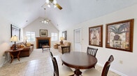 Located at 46 Hampton Cir in Warner Robins, Georgia, this single-floor space is thoughtfully designed to maximize its compact footprint. The open-plan layout seamlessly connects the living room, dining area, and kitchen, creating an efficient and cohesive interior.

The living room is a standout feature, anchored by a wood-framed fireplace flanked by two windows that allow natural light to brighten the space. Soaring vaulted ceilings with dual ceiling fans add a sense of vertical openness, making the room feel notably more spacious than its footprint suggests. Neutral-toned carpet and light walls contribute to an airy, welcoming ambiance.

Adjacent to the living room, the dining area accommodates a round dining table and chairs and benefits from the same vaulted ceiling line. Decorative framed artwork adorns the walls, adding character to the space. A pass-through counter connects the dining area directly to the kitchen, enhancing the open feel.

The kitchen features warm honey-toned wood cabinetry, a black range, a refrigerator, and a dishwasher, with a light-toned countertop and tile flooring continuing throughout. The layout is practical and well-organized, offering functional storage and workspace within a compact footprint.