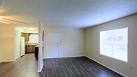 Located at 4612 Spring Hill Ave. in Mobile, Alabama, this single-floor unit offers a clean and functional layout designed for comfortable everyday living. The living area is highlighted by rich, dark hardwood-style flooring that runs throughout, providing a warm contrast to the light-toned walls and textured ceiling above. Natural light filters in through windows on multiple sides of the room, creating a bright and welcoming atmosphere. A partial dividing wall with a decorative post separates the living space from the kitchen area, maintaining an open and connected feel while subtly defining each zone. The kitchen is equipped with cabinetry and a sink, and benefits from its own window, allowing for additional natural light and ventilation. A private entry door is centrally positioned, adding to the practicality of the layout. The neutral wall tones throughout provide a versatile backdrop, making the space easy to personalize. Overall, the unit presents a straightforward and well-maintained interior with durable finishes suited for daily use.