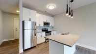 Located at 223 E Town St in the heart of Columbus, Ohio, this single-floor space offers a clean, contemporary design throughout. The kitchen serves as a standout feature, showcasing crisp white shaker-style cabinetry that extends to the ceiling for ample storage, complemented by stainless steel appliances including a refrigerator, gas range, and built-in microwave. A central island with a dark quartz countertop provides additional prep space and is equipped with an undermount sink, making it both functional and visually striking. A trio of sleek black pendant lights hang above the island, adding a modern, industrial touch to the space. Light wood-tone flooring runs throughout, lending warmth and continuity to the interior. The neutral gray and white color palette creates a bright, airy atmosphere that feels open and inviting. The overall design reflects a modern aesthetic with thoughtful attention to detail, making this a well-appointed space ideally situated in downtown Columbus within close proximity to local dining, entertainment, and business districts.
