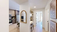 Located at 205 Hartell Way SE in Calgary, Alberta, this thoughtfully designed 2-bedroom, 3-bathroom residence offers a functional and stylish single-floor layout. The open-concept kitchen and living room serve as the heart of the home, where the kitchen impresses with two-tone cabinetry — warm wood-grain lowers paired with light upper cabinets — a bold iridescent tile backsplash, quartz countertops, and stainless steel appliances including a range, over-the-range microwave, and refrigerator. Light hardwood flooring runs throughout, adding warmth and continuity. The living room is bright and welcoming, with a sliding glass door that opens to a private balcony offering outdoor views. The primary bedroom features direct access to a well-appointed ensuite bathroom with a dual-sink vanity, wood cabinetry, quartz countertops, and a dedicated walk-in closet complete with built-in shelving. The second bedroom is a comfortable space with a built-in closet. Each bathroom is finished with framed mirrors, black hardware accents, and clean neutral tones. A hallway connects all spaces efficiently, maintaining a clean, modern flow. The overall ambiance is contemporary and bright, with crisp white walls, consistent finishes, and an emphasis on practical elegance throughout.