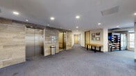 Located at 445 Oakland St in Morgantown, WV, this expansive amenity floor spans a generous footprint designed to offer residents a comprehensive suite of shared spaces. The welcoming entrance opens into a well-appointed lounge area featuring warm hardwood flooring, a striking floor-to-ceiling tile accent wall housing a sleek linear electric fireplace, and curated furnishings including a tufted leather sofa, egg chair, and cowhide rug. A secondary lounge nook with large windows provides natural light and access to an outdoor seating area alongside a pool table and vending machines, creating an inviting social hub. The private theater room impresses with tiered, luxury leather recliner seating, atmospheric LED lighting, and dark, immersive décor accented by film reel wall art. The fitness center is equipped with free weights, weight benches, cable machines, and full-length mirrors set against bold teal walls and multi-toned carpet tile. Wide, well-lit hallways with patterned carpet, large glass panel windows, and prominent elevator banks with stone tile surrounds ensure smooth circulation throughout the floor. Recessed lighting, a neutral color palette, and consistent modern finishes tie the entire space together into a cohesive and functional amenity experience.