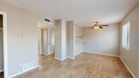 This single-floor space offers a functional and straightforward layout designed for comfortable everyday living. The main living area is open and airy, featuring light wood-look flooring that flows consistently throughout the unit. Painted concrete block walls add a distinctive architectural texture, complemented by neutral warm-gray tones on the painted surfaces. A ceiling fan with a light fixture provides both ventilation and ambient lighting, while a built-in pass-through counter connects the living space to the kitchen area, enhancing the open feel.

The galley-style kitchen is efficiently arranged with white cabinetry lining both sides, offering ample storage. It includes a gas range, a full-size refrigerator, and a sink, all finished in white. The continuation of wood-look flooring ties the kitchen seamlessly to the rest of the space.

The bedroom is well-proportioned and bright, benefiting from a large window that brings in natural light and views of the surroundings. A ceiling fan mirrors the living area's fixture, and the same consistent flooring carries through. A louvered door leads to a closet, providing practical storage.

The bathroom is clean and functional, featuring a single vanity with a countertop sink, mirrored cabinet, a tiled tub-shower combination, and a toilet. Textured ceilings are present throughout, and the unit also includes visible HVAC vents for climate control.