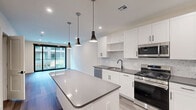 Located at 630 Washington Avenue in Belleville, NJ, this modern one-bedroom, one-bathroom unit offers a thoughtfully designed layout with contemporary finishes throughout. The open-concept kitchen and living area serves as the heart of the space, anchored by a sleek center island with a dark quartz countertop and stylish pendant lighting overhead. The kitchen is outfitted with crisp white shaker cabinetry, a decorative mosaic tile backsplash, dark countertops, stainless steel appliances including a gas range, built-in microwave, dishwasher, and refrigerator, and a matte black faucet — all complemented by wood-look flooring that flows throughout. The living area opens to the outdoors through a floor-to-ceiling sliding glass door, allowing abundant natural light and views of the surrounding courtyard and building exterior. A large picture window further enhances the sense of openness. The well-proportioned bedroom features neutral walls, recessed lighting, and the same wood-look flooring. A dedicated closet provides organized storage. The bathroom showcases large-format dark tile work, adding a bold, modern contrast to the otherwise light and airy palette. A hallway connects the private quarters, maintaining a clean, functional flow throughout the unit.