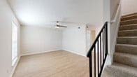 This two-story home offers a practical and comfortable layout spread across two evenly balanced floors. The main level features a combined dining and living area with light hardwood-style flooring, soaring ceilings, and a ceiling fan with integrated lighting. Large windows fitted with white horizontal blinds allow natural light to fill the space, while a sleek black-railed staircase connects to the upper level. The kitchen is efficiently designed with white shaker-style cabinetry, black hardware, a stainless steel refrigerator, an electric range, and a single-basin sink beneath a window — all tied together with matching light wood flooring. Three full bathrooms are found throughout the home, each featuring clean white tile tub-shower combinations with brushed gold fixtures, maintaining a consistent and tidy aesthetic. The three bedrooms are generously proportioned, including a spacious primary suite. Bedrooms feature a mix of light wood flooring and plush carpeting, with ceiling fans, natural window light, and neutral wall tones creating a calm and restful atmosphere. The upper floor is accessible via a carpeted staircase and mirrors the lower level's efficient use of space. Throughout, the home maintains a clean, neutral palette that is both welcoming and move-in ready.