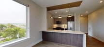 This thoughtfully designed single-floor unit at 222 Avenue E in Bayonne, NJ offers a clean, modern aesthetic throughout. Light-toned hardwood flooring flows consistently across the living areas and bedrooms, creating a cohesive and polished look. Large windows in multiple rooms invite abundant natural light while framing views of the surrounding Bayonne neighborhood and nearby greenery.

The open-concept kitchen is a standout feature, showcasing dark wood cabinetry paired with sleek upper cabinets in a lighter finish, white quartz countertops, and stainless steel appliances including a gas range, built-in microwave, and refrigerator. A peninsula with pendant lighting overhead connects the kitchen to the living area, making it well-suited for entertaining. A large window beside the kitchen provides additional natural light.

The bedrooms are generously sized, each with wide windows offering elevated outdoor views. Recessed lighting and flush-mount fixtures provide flexible illumination throughout.

The bathroom features large-format beige tile flooring, marble-effect wall tile, a wall-mounted dark wood vanity, a round mirror, and chrome fixtures, delivering a refined, spa-like atmosphere. The overall design reflects a contemporary luxury aesthetic with high-quality finishes throughout.