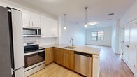 Located at 1 North Main Street in Port Chester, NY, this thoughtfully designed one-bedroom, one-bathroom residence offers a modern living experience with a clean, contemporary aesthetic throughout. Light wood-tone flooring flows seamlessly across the open-concept floor plan, connecting the kitchen, dining, and living areas into one cohesive space.

The kitchen is a standout feature, outfitted with stainless steel appliances including a refrigerator, electric range, microwave, and dishwasher. A peninsula with a quartz countertop and an undermount sink serves as both a functional workspace and a casual dining area. White upper cabinetry is paired with warm wood-toned lower cabinets, complemented by a classic subway tile backsplash. Pendant lighting above the peninsula adds a stylish accent.

The living and dining area benefits from natural light through a large window with views of the surrounding neighborhood. The bedroom is a comfortable size, featuring its own window with an outdoor view and direct access to a walk-in closet with wire shelving.

The bathroom is finished with large-format tile flooring, a wood-toned vanity with a white countertop, an illuminated mirror, and a full soaking tub with a tile surround. Additional highlights include four closets total, a dedicated laundry area, and a crisp, neutral palette throughout.
