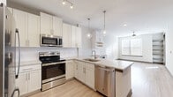 This thoughtfully designed single-floor residence offers a cohesive blend of modern finishes and functional living spaces. The kitchen is a standout feature, showcasing crisp white shaker cabinetry, light quartz countertops, a subway tile backsplash, and a full suite of stainless steel appliances including a range, microwave, dishwasher, and refrigerator. A peninsula with pendant lighting overhead adds both workspace and visual elegance, while light hardwood-style flooring ties the space seamlessly into the adjacent living area. The living space is bright and open, with natural light streaming through blinds-fitted windows and light flooring underfoot. The bedrooms are carpeted and well-lit, each featuring ceiling fans and windows that invite natural light. One bedroom includes a walk-in closet outfitted with wire shelving for ample storage. The primary bathroom is refined and spacious, featuring a double-sink vanity with white cabinetry, quartz countertops, and a glass-enclosed tile shower with brushed nickel fixtures. A dedicated mudroom near the entry provides practical built-in bench seating, wall hooks, and cubbies — an ideal drop zone finished in warm greige tones. Throughout, the residence maintains a clean, neutral palette with consistent trim details and modern hardware.