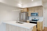 This thoughtfully designed one-bedroom, one-bathroom unit offers a bright and contemporary living experience across a single floor. The open-concept kitchen and living area serves as the heart of the home, featuring light wood cabinetry, crisp white quartz countertops, and a full suite of stainless steel appliances including a French door refrigerator, electric range, and built-in microwave. A peninsula with an undermount sink and sleek pendant lighting above doubles as a breakfast bar, seamlessly connecting the kitchen to the living space. Wide-plank hardwood flooring flows throughout the main living areas, complemented by recessed lighting and ceiling fans that enhance both comfort and style. Large windows flood the living room with natural light and offer open outdoor views. The spacious primary bedroom is fitted with plush carpet, a ceiling fan, and a sliding glass door that opens to a private balcony with scenic views. The bathroom is clean and functional, featuring a full soaking tub and shower combination with brushed nickel fixtures. Throughout the unit, a neutral color palette, modern finishes, and an efficient layout create a cohesive, move-in-ready atmosphere.