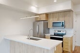 This thoughtfully designed one-bedroom, one-bathroom unit offers a bright and contemporary living experience across a single floor. The open-concept kitchen and living area serves as the heart of the home, featuring light wood cabinetry, crisp white quartz countertops, and a full suite of stainless steel appliances including a French door refrigerator, electric range, and built-in microwave. A peninsula with an undermount sink and sleek pendant lighting above doubles as a breakfast bar, seamlessly connecting the kitchen to the living space. Wide-plank hardwood flooring flows throughout the main living areas, complemented by recessed lighting and ceiling fans that enhance both comfort and style. Large windows flood the living room with natural light and offer open outdoor views. The spacious primary bedroom is fitted with plush carpet, a ceiling fan, and a sliding glass door that opens to a private balcony with scenic views. The bathroom is clean and functional, featuring a full soaking tub and shower combination with brushed nickel fixtures. Throughout the unit, a neutral color palette, modern finishes, and an efficient layout create a cohesive, move-in-ready atmosphere.