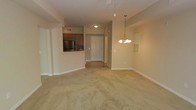 Located at 5418 Sirius Dr in Wilmington, NC, this single-floor residence offers a thoughtfully arranged open-concept layout that seamlessly connects the main living and dining areas. The living space is finished with wall-to-wall carpeting in a neutral tone, creating a warm and comfortable atmosphere throughout. A chandelier-style pendant light hangs over the dining area, adding a decorative touch to the open floor plan.

The kitchen is positioned adjacent to the main living area and is separated by a half-wall pass-through counter, making it ideal for both cooking and entertaining. It features stainless steel appliances, including a full-size refrigerator, warm-toned cabinetry, and a ceiling-mounted light fixture. The kitchen flooring transitions to a hard surface, providing a practical and easy-to-clean workspace.

A well-lit entryway with a clean white door serves as the primary access point, with a hallway leading further into the unit. The overall color palette throughout the space is light and neutral, with beige walls and white trim contributing to a bright and airy feel. The layout is efficient and cohesive, making excellent use of the available single-floor footprint to create a functional and welcoming living environment.