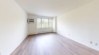 Located in Monona, WI, this single-floor, one-bedroom, two-bathroom unit offers a well-organized layout designed for comfortable everyday living. The open living room is a standout feature, showcasing light wood-style flooring, a large picture window that invites natural light and outdoor views of surrounding greenery, and a wall-mounted air conditioning unit alongside baseboard heating for year-round comfort. Adjacent to the living area, the kitchen is efficiently designed with white cabinetry extending to the ceiling for ample storage, a coil-burner electric range, an under-cabinet range hood, and a single-basin sink — all finished in a clean, neutral palette. A ceiling fan with light fixture adds airflow to the dining and kitchen area. The bedroom features plush wall-to-wall carpeting, a spacious double-door louvered closet, and warm wood-tone doors that add a classic touch. Both bathrooms are clean and functional: one includes a tub/shower combination with tiled surround, while the other features an extended white vanity countertop with built-in drawers and a large mirror. Wood-style flooring runs through the bathrooms, complementing the overall aesthetic. The unit presents a neutral, move-in-ready environment throughout.