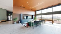 Located at 2510 W 27th Ave in Denver's vibrant LoHi neighborhood, this single-floor community lounge is a boldly designed gathering space that masterfully blends color, texture, and functionality. The interior immediately impresses with its soaring double-height ceilings, glossy terracotta-orange ceiling panels, and warm earth-toned walls that create a dramatic yet welcoming atmosphere throughout.

The main lounge area features a richly appointed seating arrangement anchored by a deep green velvet sectional sofa, complemented by a sculptural red drum side table and a patterned area rug. Adjacent to the lounge, a built-in bar and media center finished in slate blue cabinetry serves as a central focal point, framed by vertical wood slat paneling that adds warmth and architectural depth.

A spacious kitchen island with bar seating offers a communal dining and social hub, suspended above by striking hanging planters filled with lush greenery. Floor-to-ceiling windows flood the space with natural light and offer expansive views of the surrounding Denver skyline and neighboring architecture. A dedicated game area complete with a foosball table adds a playful touch. Large-format stone tile flooring grounds the entire space, tying together its eclectic, design-forward aesthetic.