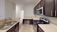 Located at 112 29th Avenue Dr NW in Hickory, North Carolina, this single-floor residence offers a practical and comfortable layout designed for everyday living. The open-concept kitchen is a standout feature, equipped with dark espresso cabinetry, light countertops, stainless steel appliances including a refrigerator, microwave, and electric range, and a peninsula that connects seamlessly to the living area. Track lighting overhead enhances the kitchen's functionality and visibility. Stone-look tile flooring runs through the kitchen, providing a durable and easy-to-maintain surface. The living area transitions to plush carpeting, creating a warm and inviting atmosphere. A built-in desk area within the kitchen space adds a convenient workspace. The bedroom is bright and comfortable, featuring soft carpet flooring and a large window with horizontal blinds that allows natural light to filter in while offering views of the surrounding greenery. The bathroom is well-appointed with a wide vanity, dark cabinetry with brushed nickel hardware, a large mirror, and tile flooring that complements the rest of the home. A closet with double doors provides ample storage within the bathroom area. The overall design features neutral tones throughout, creating a cohesive and move-in-ready living environment.