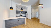 Located at 2801 S Pennsylvania St in Indianapolis, this thoughtfully designed one-bedroom, one-bathroom unit offers a well-appointed single-floor layout with modern finishes and impressive architectural details throughout. Soaring ceilings and warm wood-look plank flooring create an open, airy atmosphere from the moment you enter.

The kitchen is a standout feature, showcasing a striking waterfall quartz island with an undermount sink and matte black faucet, complemented by charcoal gray cabinetry, a bold geometric patterned tile backsplash, and a full suite of stainless steel appliances. Stylish black pendant lights with gold interiors add a contemporary touch, while recessed lighting ensures bright, even illumination throughout the open living area.

The spacious primary bedroom benefits from multiple windows that invite natural light and includes access to a well-organized walk-in closet outfitted with a modular black shelving and drawer system. The bathroom features marble-look hexagonal tile flooring, a full tub/shower combination with oil-rubbed bronze fixtures, and a dark-toned vanity topped with a round mirror. Clean white walls and crisp black hardware details tie the design together cohesively across every room, delivering a polished and modern living environment.