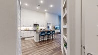 This well-appointed 2-bedroom, 3-bathroom residence is designed with a modern aesthetic, combining functionality and style across a single floor. The open-concept layout connects the kitchen and living areas seamlessly, creating an inviting, cohesive space ideal for both everyday living and entertaining.

The kitchen is a standout feature, showcasing crisp white shaker cabinetry, dark granite countertops, a white subway tile backsplash, and stainless steel appliances. A central island with an integrated sink and bar seating serves as both a practical workspace and a social hub. Built-in shelving near the kitchen entry adds additional storage and display space.

The living room features notably high ceilings and large windows that allow generous natural light to fill the space. Wood-look flooring runs consistently throughout, contributing to a warm and unified feel.

Both bedrooms are comfortably scaled and receive natural light through large windows with outdoor views. Each bedroom benefits from its own dedicated walk-in closet with multi-tier hanging rods and wood-look flooring. The primary bedroom connects directly to an en-suite bathroom featuring a dark granite vanity, a frameless glass shower, and clean white cabinetry. Additional bathrooms include tub-shower combinations with white subway tile surround and matching dark-countered vanities.