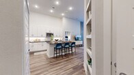 This well-appointed 2-bedroom, 3-bathroom residence is designed with a modern aesthetic, combining functionality and style across a single floor. The open-concept layout connects the kitchen and living areas seamlessly, creating an inviting, cohesive space ideal for both everyday living and entertaining.

The kitchen is a standout feature, showcasing crisp white shaker cabinetry, dark granite countertops, a white subway tile backsplash, and stainless steel appliances. A central island with an integrated sink and bar seating serves as both a practical workspace and a social hub. Built-in shelving near the kitchen entry adds additional storage and display space.

The living room features notably high ceilings and large windows that allow generous natural light to fill the space. Wood-look flooring runs consistently throughout, contributing to a warm and unified feel.

Both bedrooms are comfortably scaled and receive natural light through large windows with outdoor views. Each bedroom benefits from its own dedicated walk-in closet with multi-tier hanging rods and wood-look flooring. The primary bedroom connects directly to an en-suite bathroom featuring a dark granite vanity, a frameless glass shower, and clean white cabinetry. Additional bathrooms include tub-shower combinations with white subway tile surround and matching dark-countered vanities.