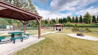 Located at 970 Windy Hill Rd SE in Smyrna, Georgia, this outdoor community amenity space centers around a generously sized swimming pool with clear, turquoise water. The pool is framed by a wide concrete deck that provides ample room for lounging and socializing. Safety features are prominently in place, including pool markers and posted pool rules signage along the perimeter fence.

The area is enclosed by a classic black wrought-iron fence, offering both security and an open, airy feel. Within the enclosure, a covered gazebo with a dark umbrella canopy provides a shaded retreat for relaxing out of the sun. Seating with umbrella-shaded tables is also available along the deck perimeter.

A children's playground equipped with slides and climbing structures is situated just beyond the pool fence, making this a family-friendly destination. Mature trees, including tall pines and deciduous varieties displaying seasonal color, surround the space and provide a natural, park-like backdrop.

A utility building adjacent to the pool houses additional facilities, and landscaped plantings with ornamental grasses and shrubs add greenery throughout. The overall ambiance is welcoming and well-maintained, offering a comfortable outdoor retreat set against the backdrop of a residential community.