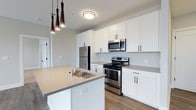 Located at 223 E Town St in the heart of Columbus, Ohio, this single-floor space offers a clean, contemporary design with thoughtful finishes throughout. The kitchen serves as a focal point of the unit, showcasing crisp white shaker-style cabinetry that extends to the ceiling, providing generous storage. Stainless steel appliances — including a French door refrigerator, gas range, and built-in microwave — complement the modern aesthetic. A central island with a single-basin sink and light quartz-style countertops adds both functionality and style, while sleek pendant lighting in a distinctive tapered design adds a decorative touch overhead. Wood-look flooring runs throughout, adding warmth and continuity to the space. The layout is open and well-lit, with flush-mount ceiling lighting enhancing brightness. The neutral color palette of soft whites and warm grays creates a versatile backdrop suitable for a variety of interior styles. Situated in downtown Columbus, this space benefits from its central urban location, offering convenient access to the city's dining, entertainment, and business districts.