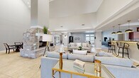 Located at 8001 W Parkway Blvd in Sand Springs, Oklahoma, this expansive single-story space offers a generous and versatile layout designed for both gathering and relaxation. The centerpiece of the main living area is a dramatic floor-to-ceiling stone fireplace, flanked by soaring vaulted ceilings that lend an airy, grand atmosphere. Large-format tile flooring flows throughout the open-plan common areas, seamlessly connecting the various functional zones.

The full kitchen is outfitted with rich cherry wood cabinetry, granite countertops, a central island, and a tray ceiling with recessed lighting. High transom windows allow natural light to pour in, brightening the workspace. Adjacent to the kitchen, a formal dining area features similarly elevated ceilings, enhancing the sense of volume.

A dedicated lounge or media room provides carpeted comfort with recessed lighting and direct views to the outdoors. The game room is a standout feature, equipped with a pool table, shuffleboard, wall-mounted television, and expansive windows overlooking an outdoor pool area. A quieter sitting room with neutral tones and built-in media storage rounds out the space, offering a more relaxed retreat. Together, these areas create a well-appointed, multi-functional environment ideal for community use and entertainment.
