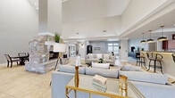Located at 8001 W Parkway Blvd in Sand Springs, Oklahoma, this expansive single-story space offers a generous and versatile layout designed for both gathering and relaxation. The centerpiece of the main living area is a dramatic floor-to-ceiling stone fireplace, flanked by soaring vaulted ceilings that lend an airy, grand atmosphere. Large-format tile flooring flows throughout the open-plan common areas, seamlessly connecting the various functional zones.

The full kitchen is outfitted with rich cherry wood cabinetry, granite countertops, a central island, and a tray ceiling with recessed lighting. High transom windows allow natural light to pour in, brightening the workspace. Adjacent to the kitchen, a formal dining area features similarly elevated ceilings, enhancing the sense of volume.

A dedicated lounge or media room provides carpeted comfort with recessed lighting and direct views to the outdoors. The game room is a standout feature, equipped with a pool table, shuffleboard, wall-mounted television, and expansive windows overlooking an outdoor pool area. A quieter sitting room with neutral tones and built-in media storage rounds out the space, offering a more relaxed retreat. Together, these areas create a well-appointed, multi-functional environment ideal for community use and entertainment.
