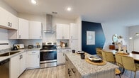 Located at 300 Hickory Trace Ln in Garner, North Carolina, this single-floor residence offers a thoughtfully designed layout that balances style and functionality throughout. The kitchen serves as a standout centerpiece, featuring crisp white shaker cabinetry, granite countertops, stainless steel appliances including an electric range with a sleek wall-mounted hood, a built-in microwave, dishwasher, and full-size refrigerator. A granite-topped island provides additional prep space and casual seating, while light wood-tone flooring ties the kitchen seamlessly into the adjoining dining and living areas. A bold navy accent wall adds a striking visual contrast to the otherwise neutral palette. The living room is generously proportioned, filled with natural light through large windows dressed with blinds and patterned drapes, and finished with wood-look flooring and a ceiling fan. The bedrooms are carpeted for comfort, each offering large windows that invite abundant daylight. The primary bedroom includes a dedicated seating area and direct access to a private ensuite. Additional bedrooms are well-sized with neutral tones and plush carpeting. Connecting hallways are finished in light hardwood-style flooring with clean, neutral walls, maintaining a cohesive and modern aesthetic throughout the entire home.
