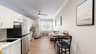 This well-appointed one-bedroom, one-bathroom unit at 2400 NE 112th Ave in Vancouver, WA offers a smart and efficient layout across a single floor. The open-concept main area seamlessly combines the living room, dining space, and kitchen into one cohesive zone. Warm hardwood-style flooring, crisp crown molding, and a ceiling fan with light fixture lend the space a clean, polished look. A large window fitted with white horizontal blinds fills the living area with natural light, complementing the neutral, soft beige walls. The kitchen is equipped with a stainless steel refrigerator and flows naturally into the dining area, which comfortably accommodates a small table and chairs. The bedroom is a well-proportioned retreat featuring a large window, crown molding, hardwood-style flooring, and a sliding-door closet offering practical storage. A second closet provides additional storage elsewhere in the unit. The bathroom is thoughtfully designed with accessibility in mind, featuring grab bars, tile surround, mosaic tile flooring, a walk-in shower with curtain, a wall-mounted cabinet, and a vanity sink. Throughout the unit, a consistent neutral palette and understated finishes create a calm, comfortable ambiance suitable for everyday living.